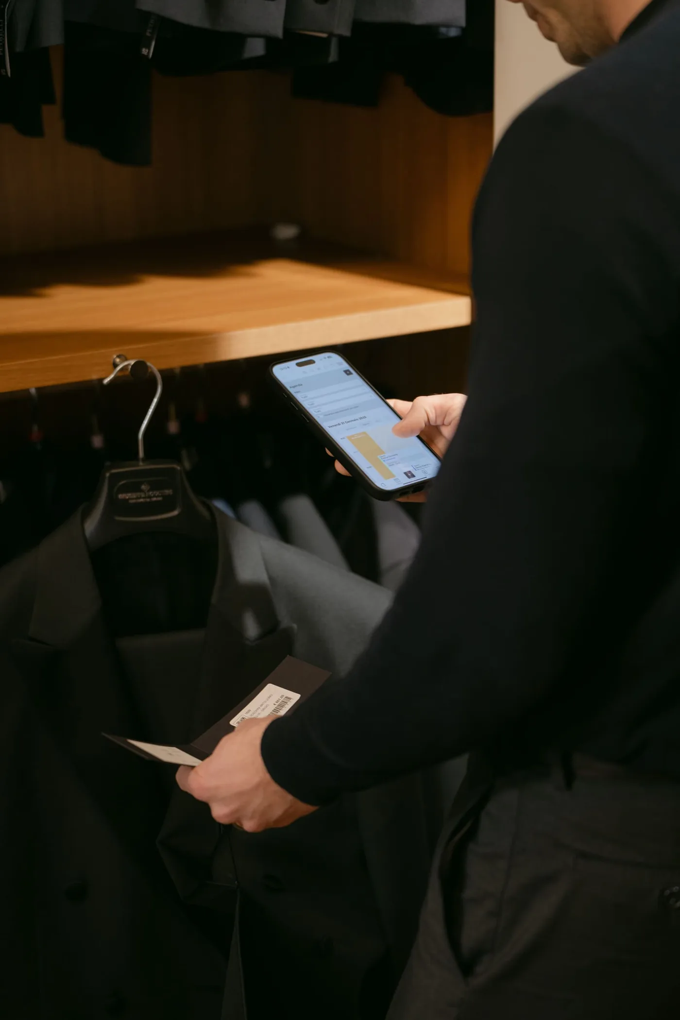 In negozio, l’agenda di Facile Atelier aperta sul telefono e, nell’altra mano, un abito appena sfilato dall’appendiabiti con il suo cartellino.
