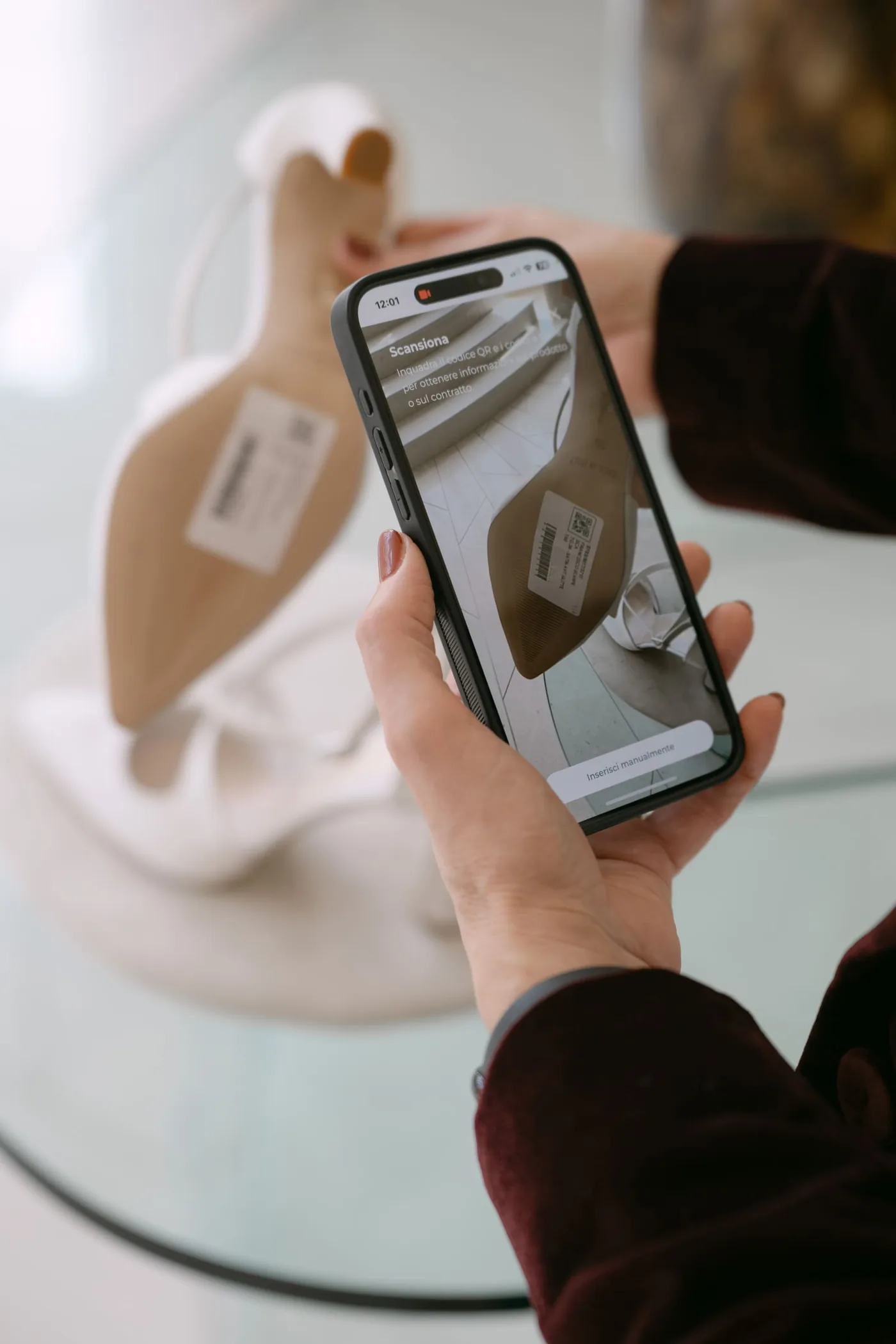 Un telefono con la schermata «Scansiona» di Facile Atelier inquadra il codice QR sull’etichetta di una scarpa da sposa appoggiata su un tavolo di vetro.